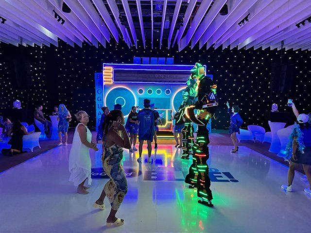 An LED-suited performer on a lit dance floor surrounded by guests